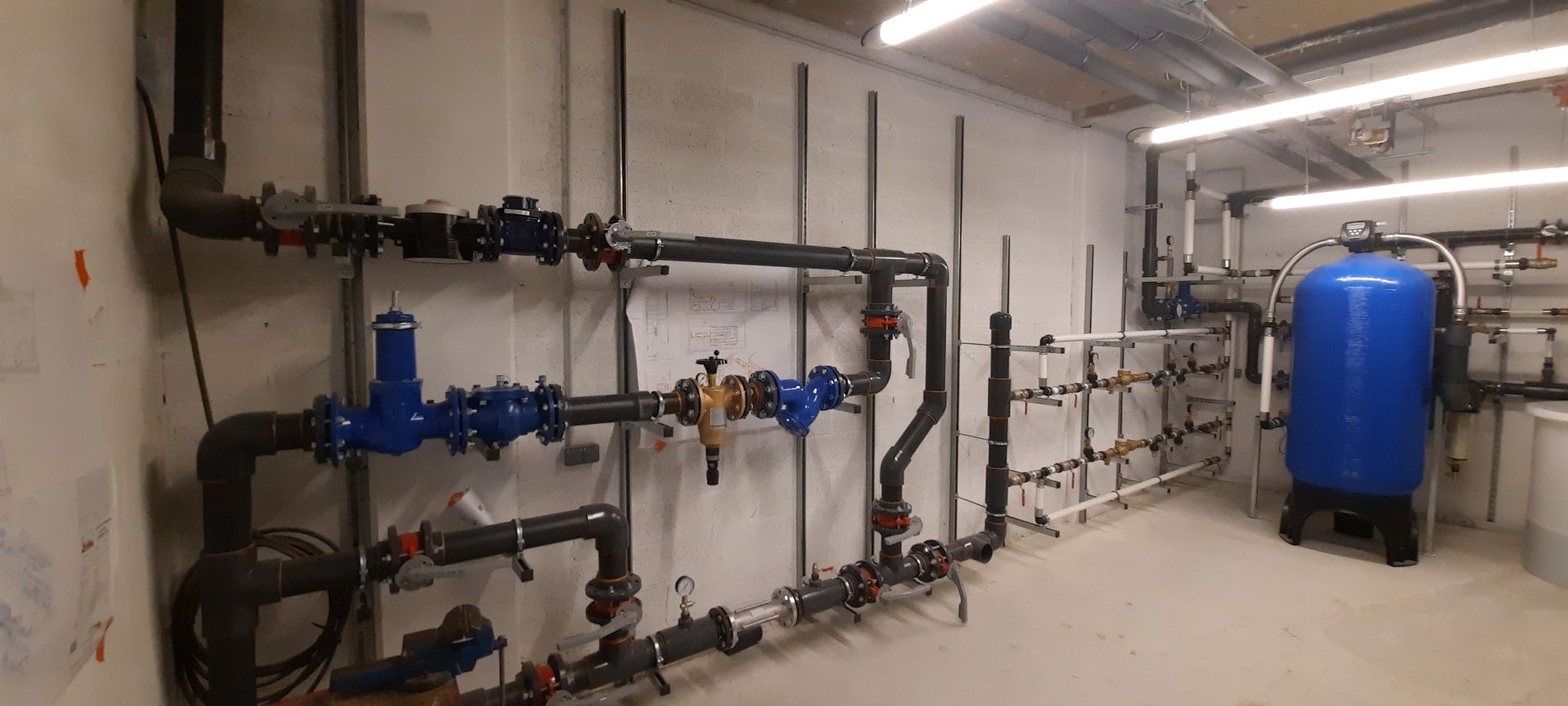 Sous-sol industriel avec réservoirs de traitement d'eau bleus, canalisations et équipements de contrôle le long du mur.