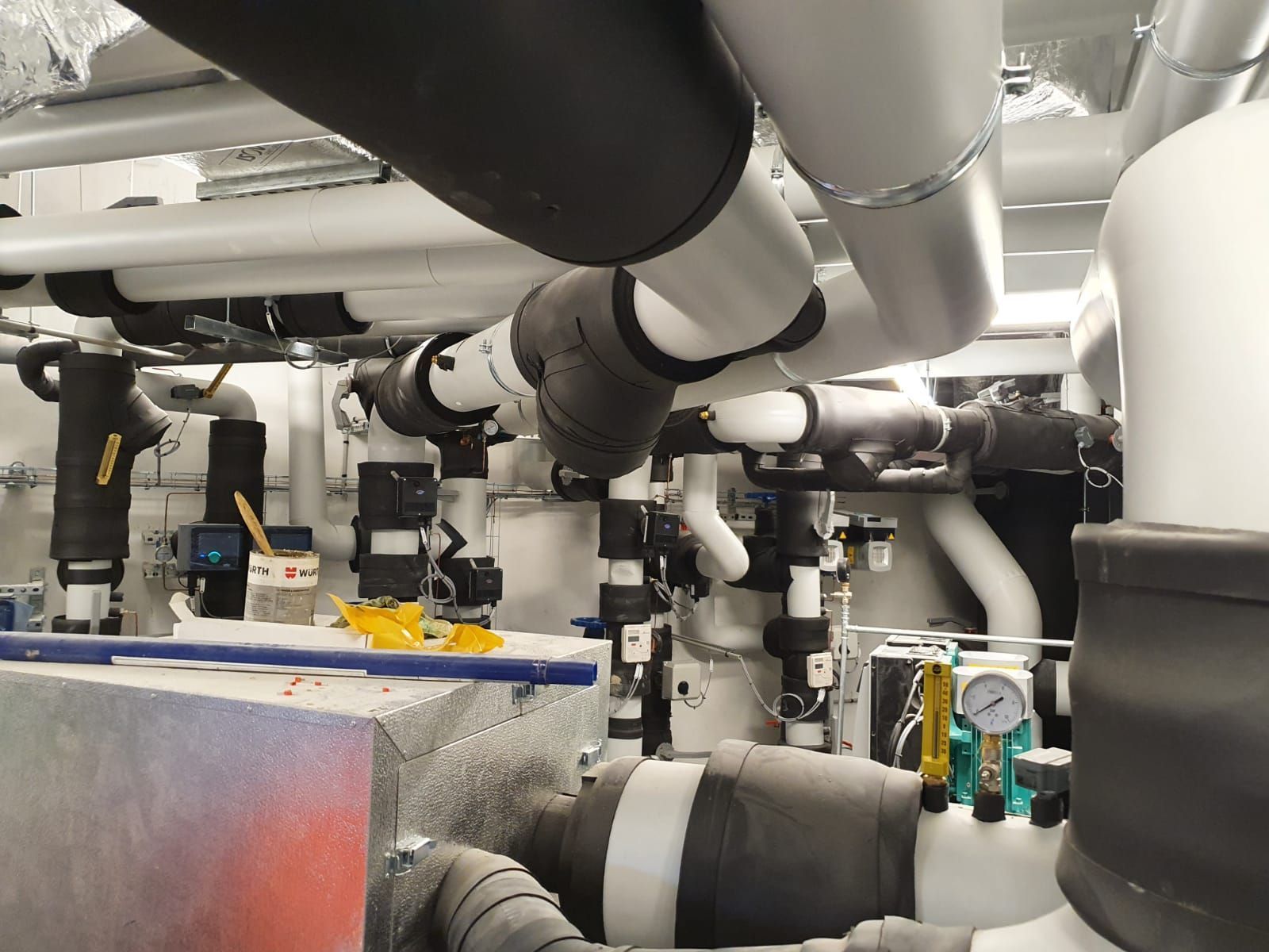 Tuyaux industriels et conduits isolés dans un local technique, avec vannes et équipements métalliques.