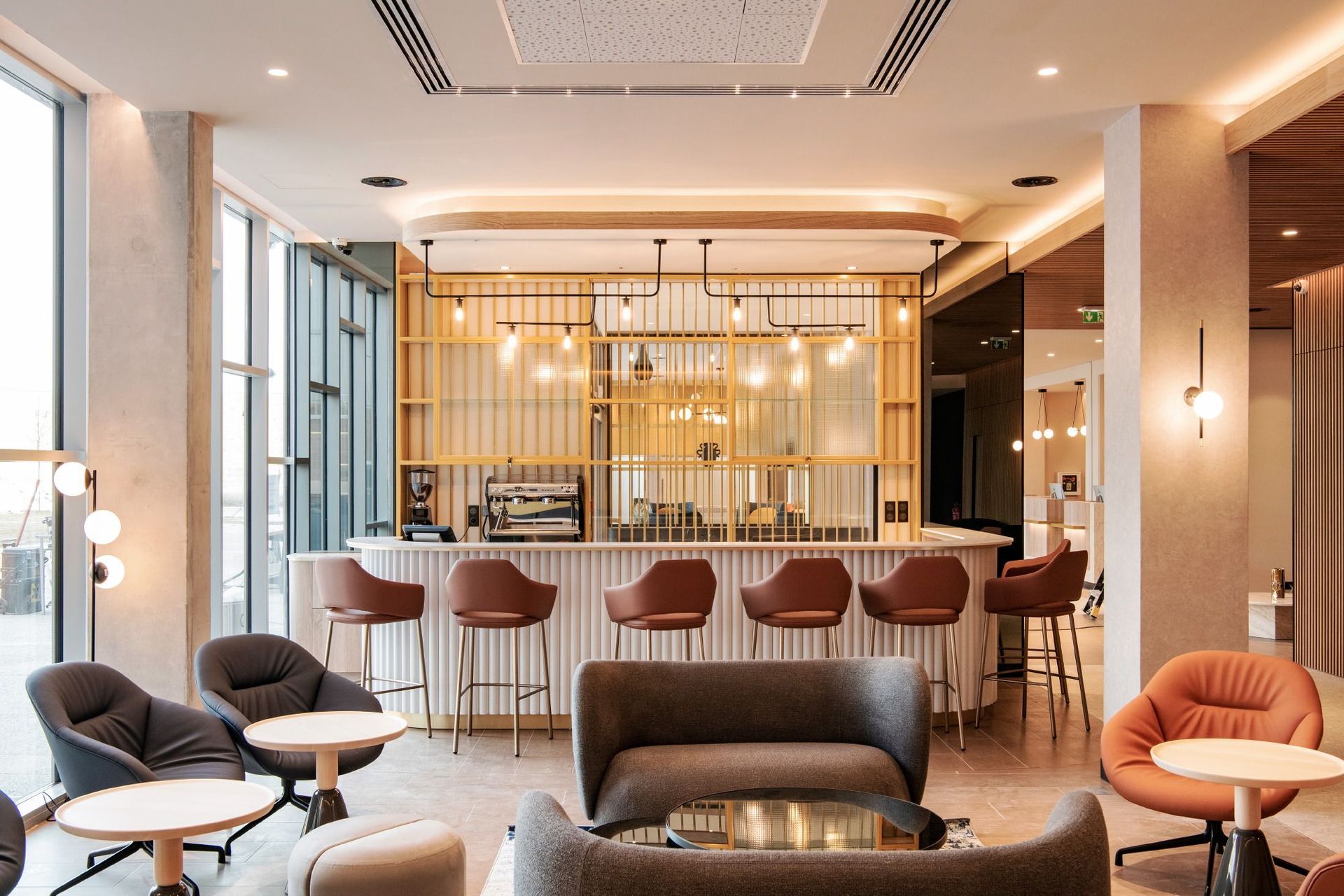 Salon d'hôtel moderne avec coin bar, accents de bois chaleureux et chaises grises et pêche