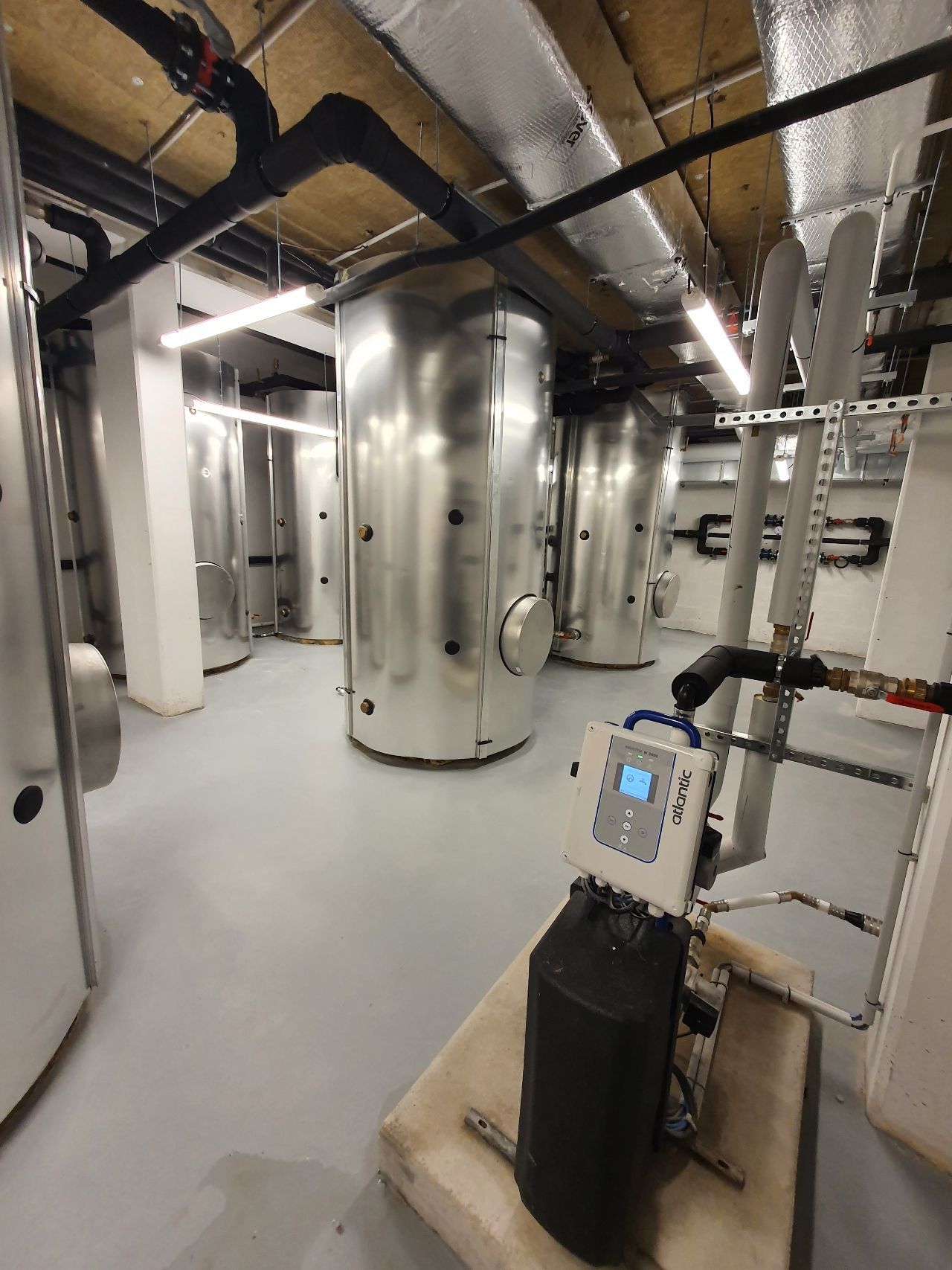 Sous-sol industriel avec de grands réservoirs d'argent, des tuyaux apparents et une unité de contrôle dans une salle des machines