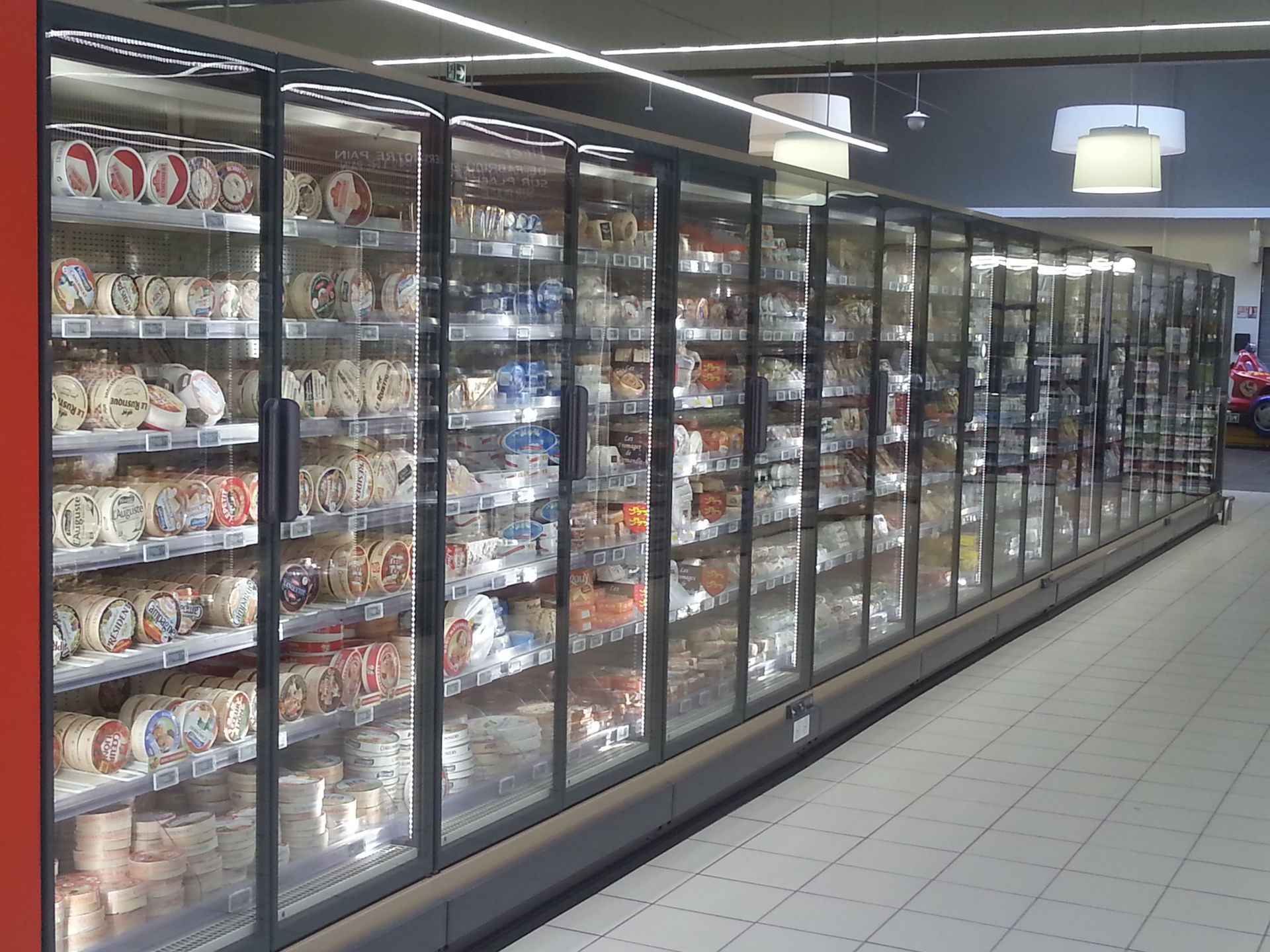 Longue allée d'épicerie avec des étagères réfrigérées à portes vitrées remplies d'aliments et de boissons emballés