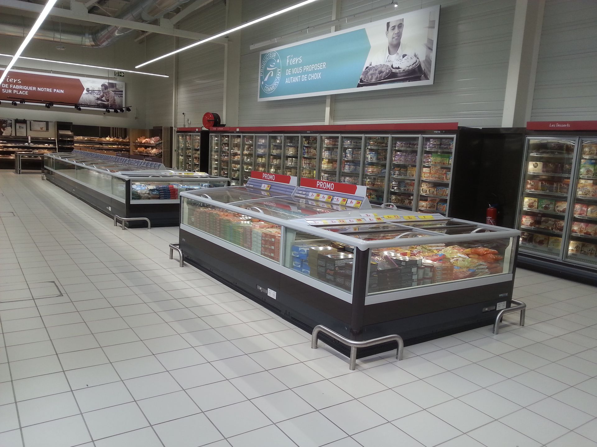 Allée vide d'un supermarché avec vitrines réfrigérées et sol carrelé