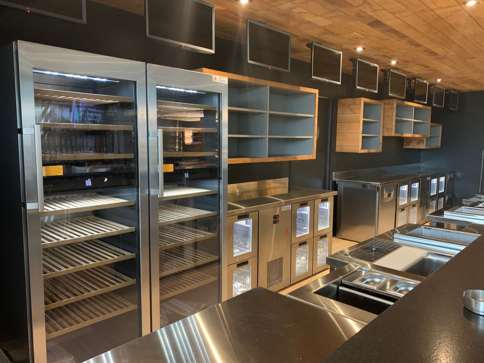 Intérieur de café moderne avec comptoirs en inox, vitrines et étagères murales sous un éclairage chaleureux