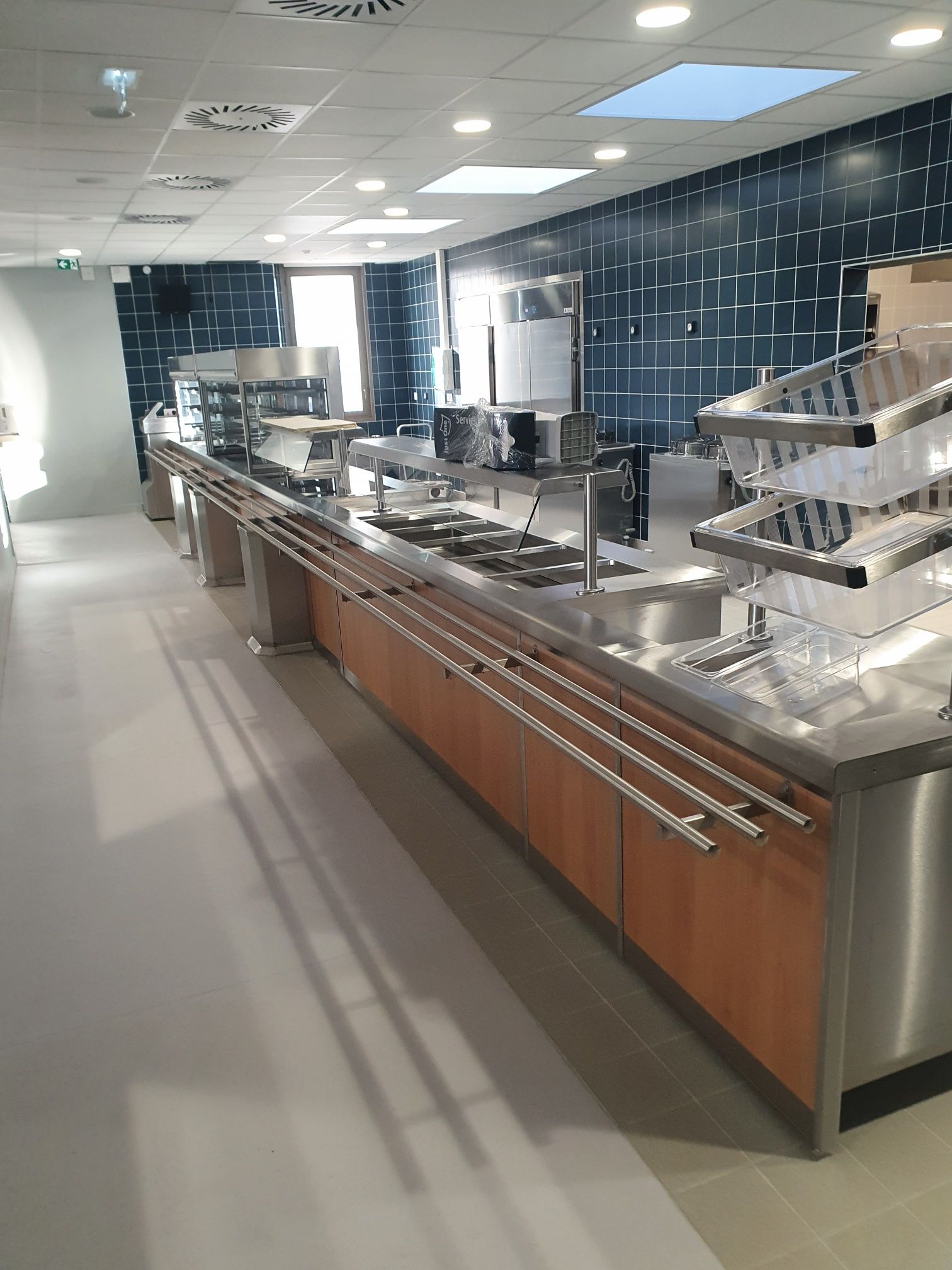 Ligne de service de cafétéria moderne avec comptoirs en acier inoxydable, armoires marron et mur carrelé noir