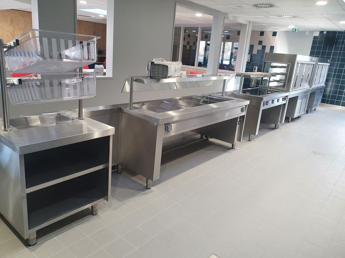 Un buffet avec des stations de service en acier inoxydable et des lampes chauffantes suspendues dans une cafétéria lumineuse