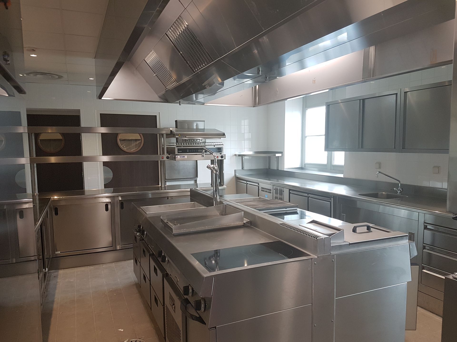 Cuisine commerciale en acier inoxydable avec postes de cuisson, fours, éviers et système de ventilation performant.