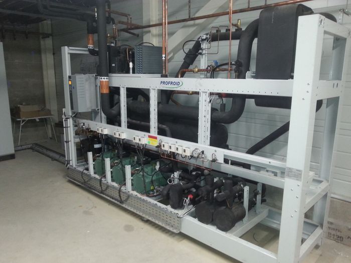 Grosse machine industrielle dans un entrepôt, avec une structure blanche, des tuyaux et des composants noirs.