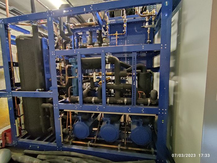 Machines industrielles bleues avec tuyaux et réservoirs à l'intérieur d'une structure métallique dans une salle utilitaire