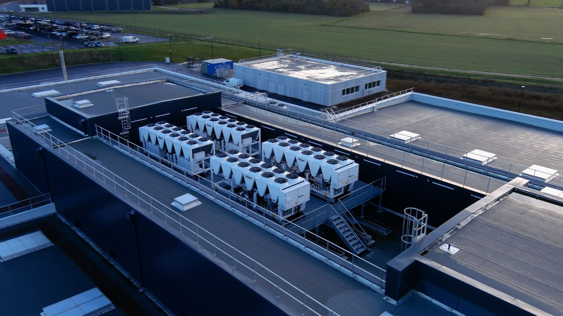 Vue aérienne d'une installation industrielle moderne avec des rangées de camions blancs et de grands entrepôts.