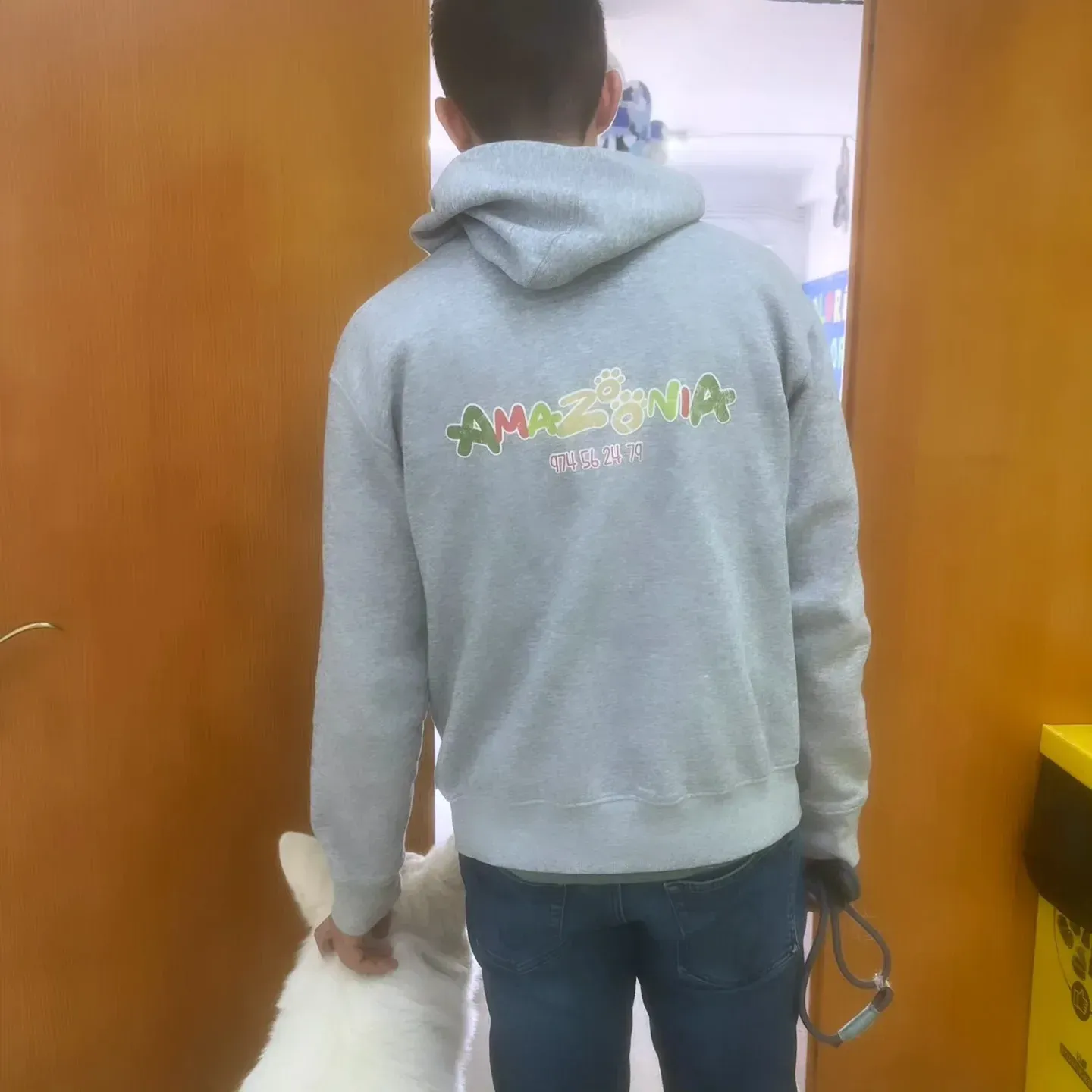 Una persona con sudadera gris y vaqueros camina por el interior llevando una bolsa blanca; se la ve de espaldas.