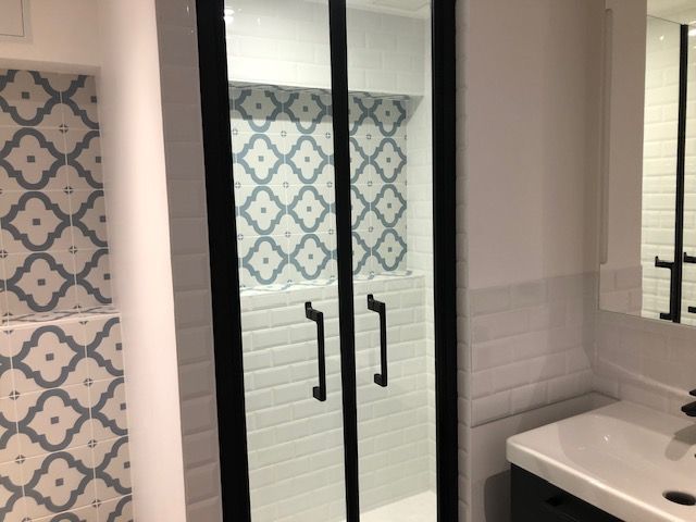 Salle de bains avec portes de douche en verre, carrelage à motifs et lavabo blanc