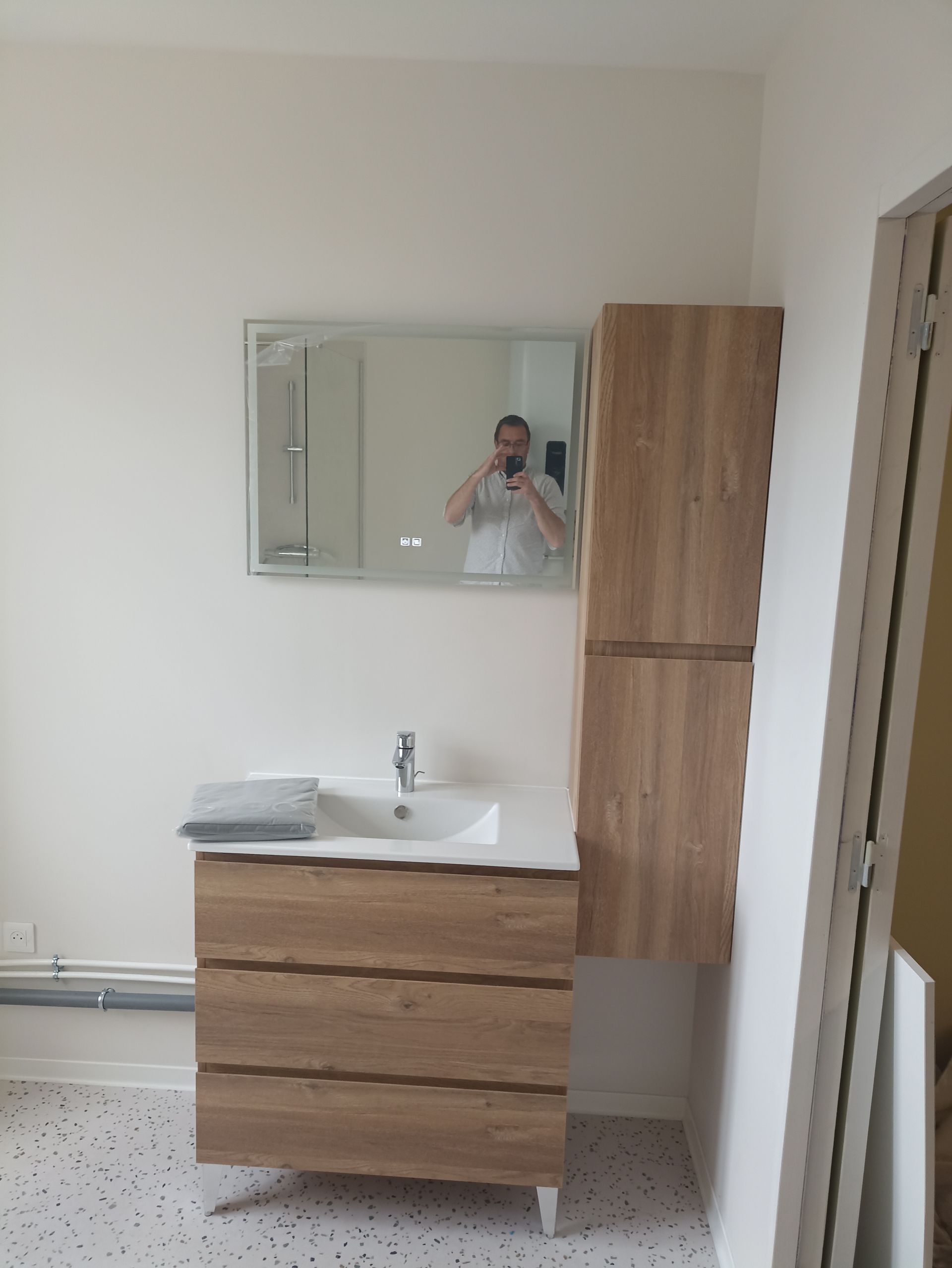 Meuble-lavabo avec miroir, tiroirs en bois et armoire haute dans une pièce beige et épurée.