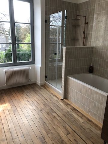 Salle de bain vide avec de grandes fenêtres, douche en verre, baignoire et parquet.