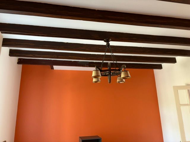 Plafond blanc avec poutres en bois foncé, un mur d'accent orange et un lustre suspendu.