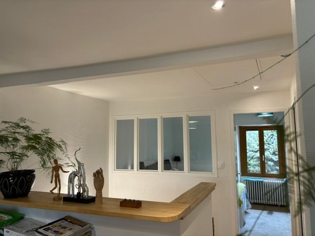 Pièce lumineuse et moderne avec murs blancs, comptoir en bois, plante en pot et fenêtres donnant sur un balcon.