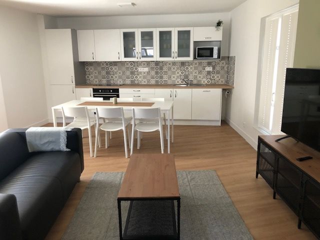 Salon moderne ouvert avec cuisine, table à manger blanche, canapé gris et meuble TV