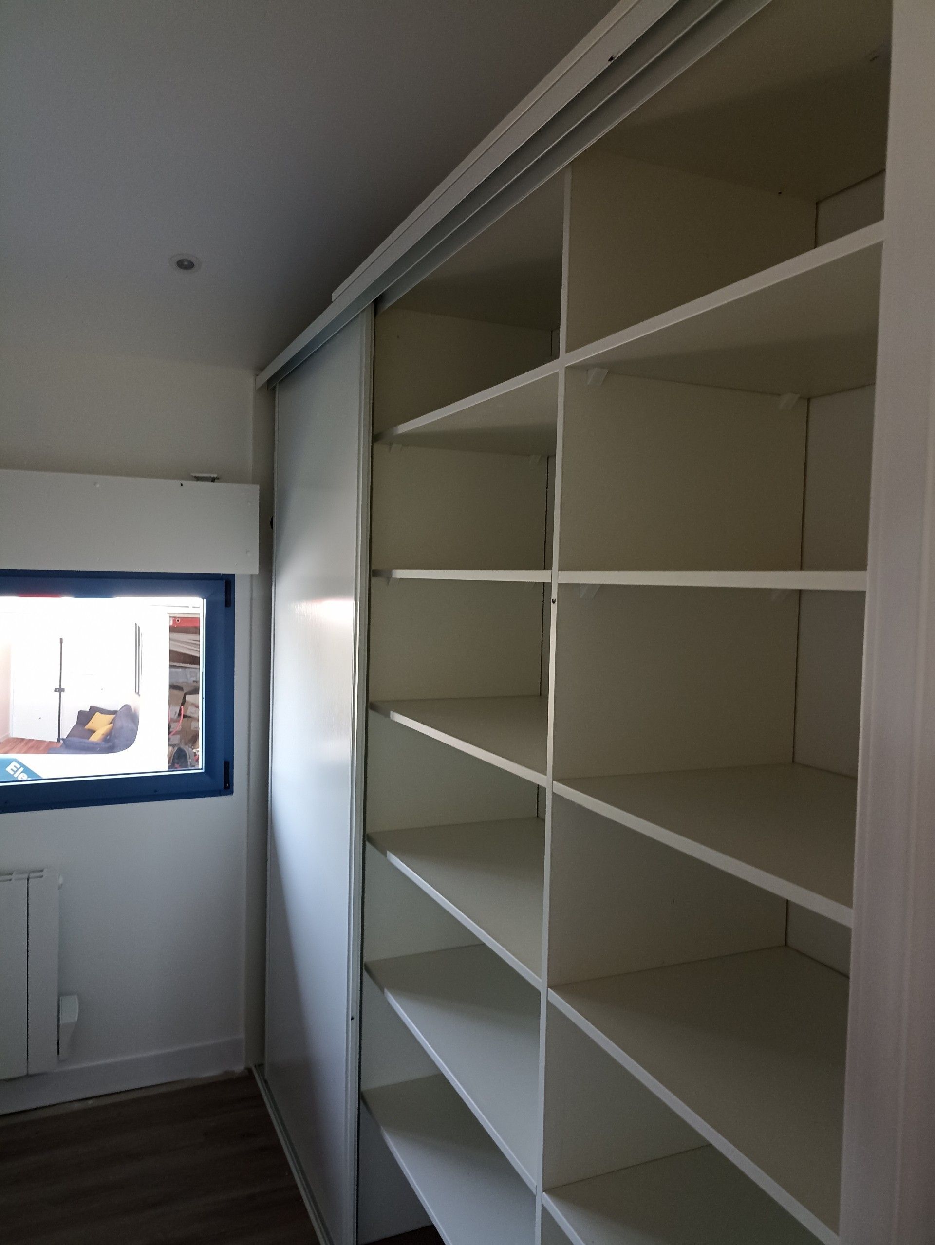 Étagères blanches encastrées dans un couloir étroit, à côté d'une fenêtre et d'une porte coulissante
