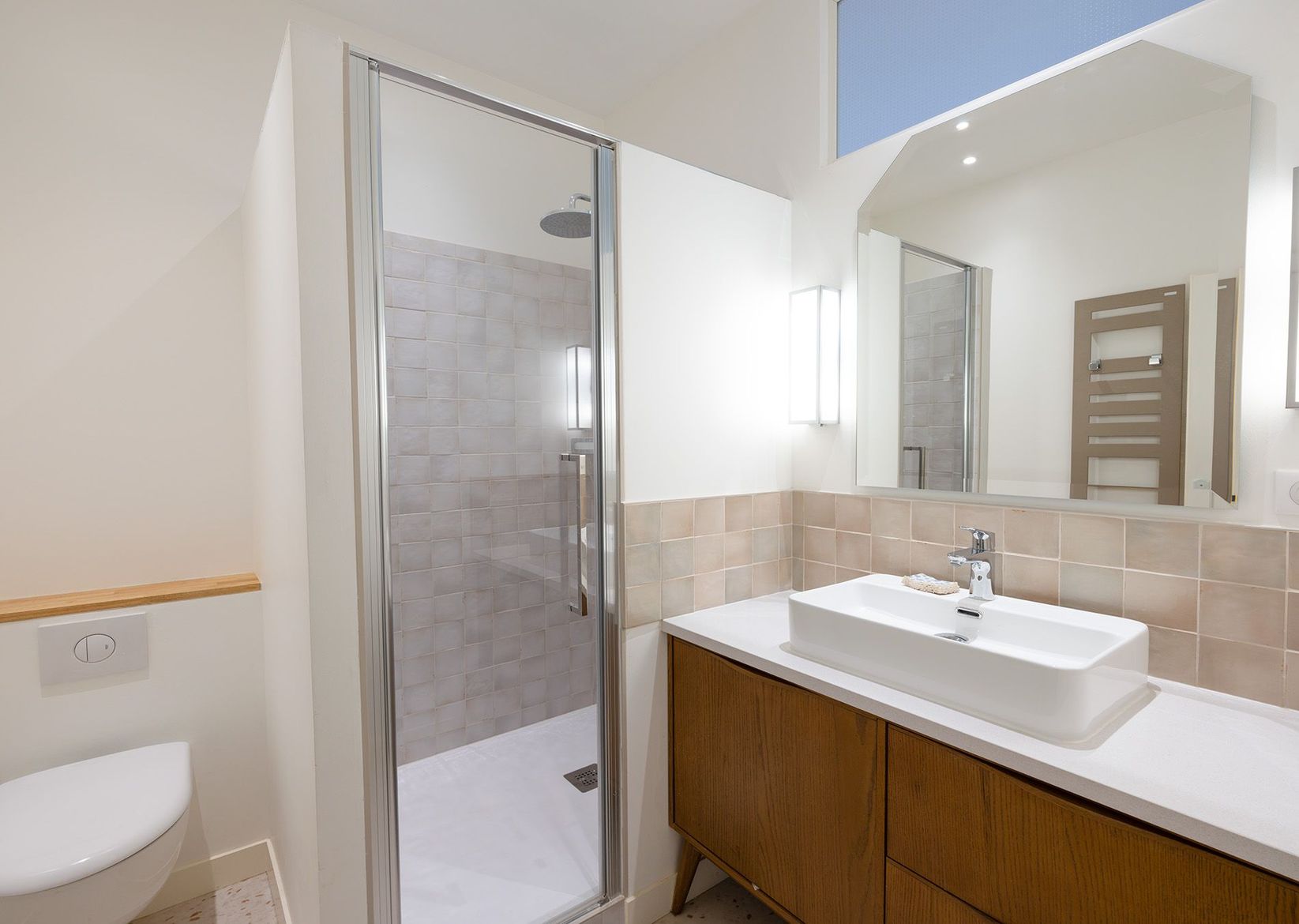 Salle de bains moderne avec douche en verre, miroir mural, lavabo blanc et serviettes rouges sur étagères ouvertes