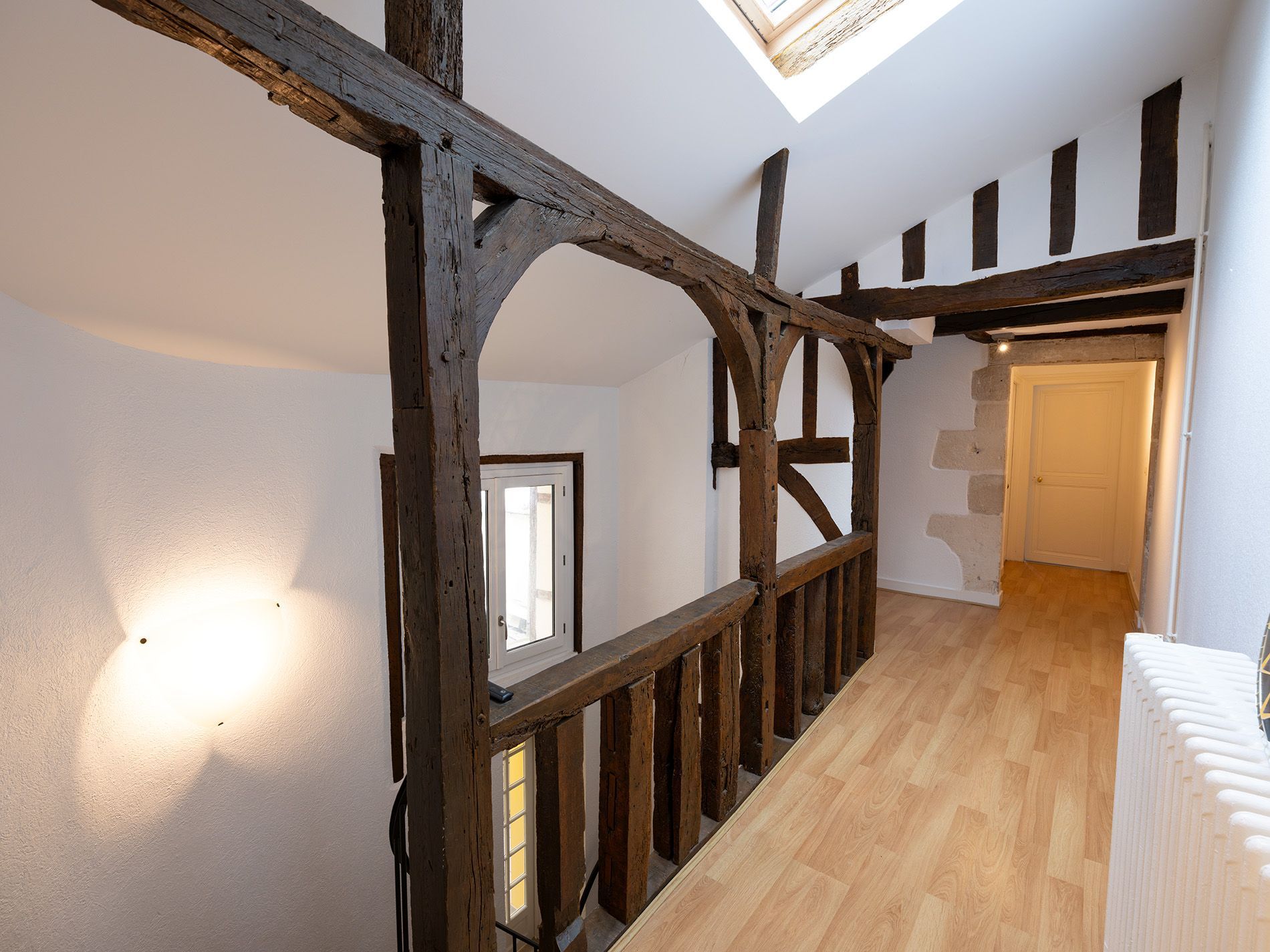 Couloir lumineux avec poutres apparentes, puits de lumière et parquet clair dans un intérieur rénové.