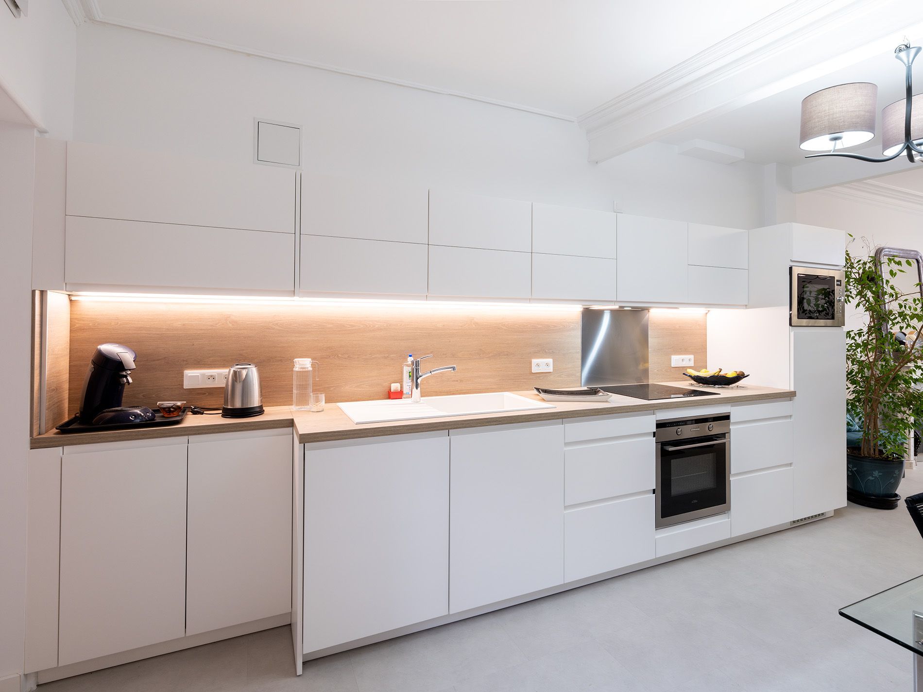 Cuisine blanche moderne avec électroménager intégré, comptoirs en bois et éclairage chaleureux sous les armoires