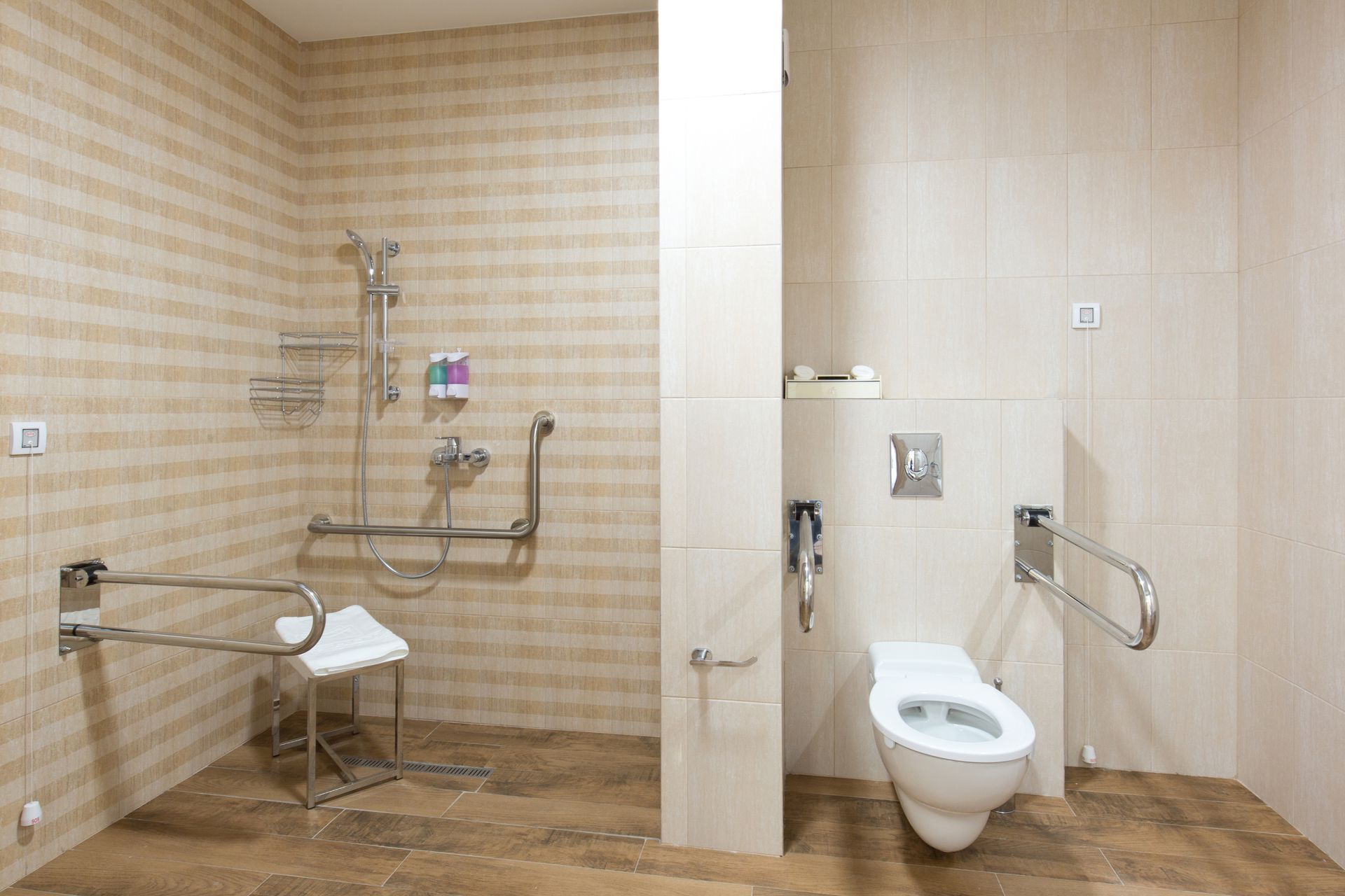 Toilettes accessibles avec douche, WC, barres d'appui et murs carrelés beiges