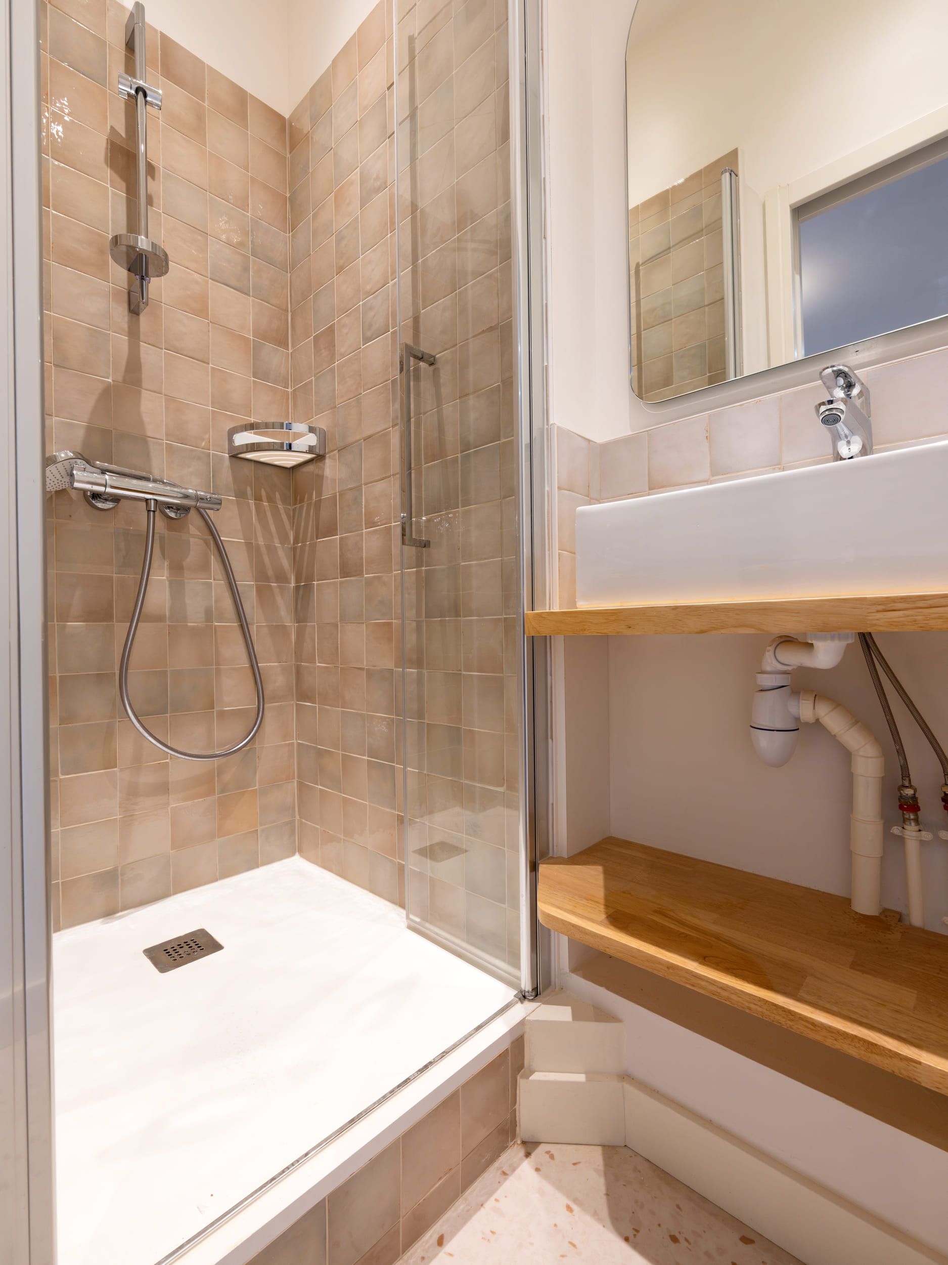 Salle de bains moderne avec douche à l'italienne en verre, murs carrelés beiges, lavabo et sèche-serviettes.