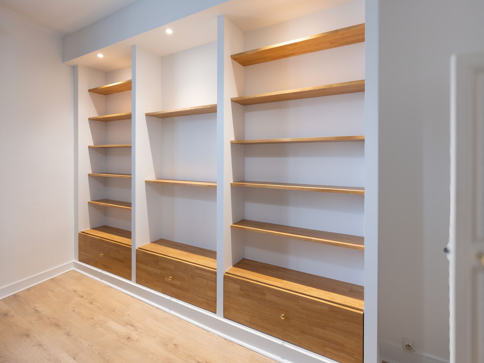 Étagères et placards en bois intégrés dans une pièce lumineuse et vide avec parquet clair