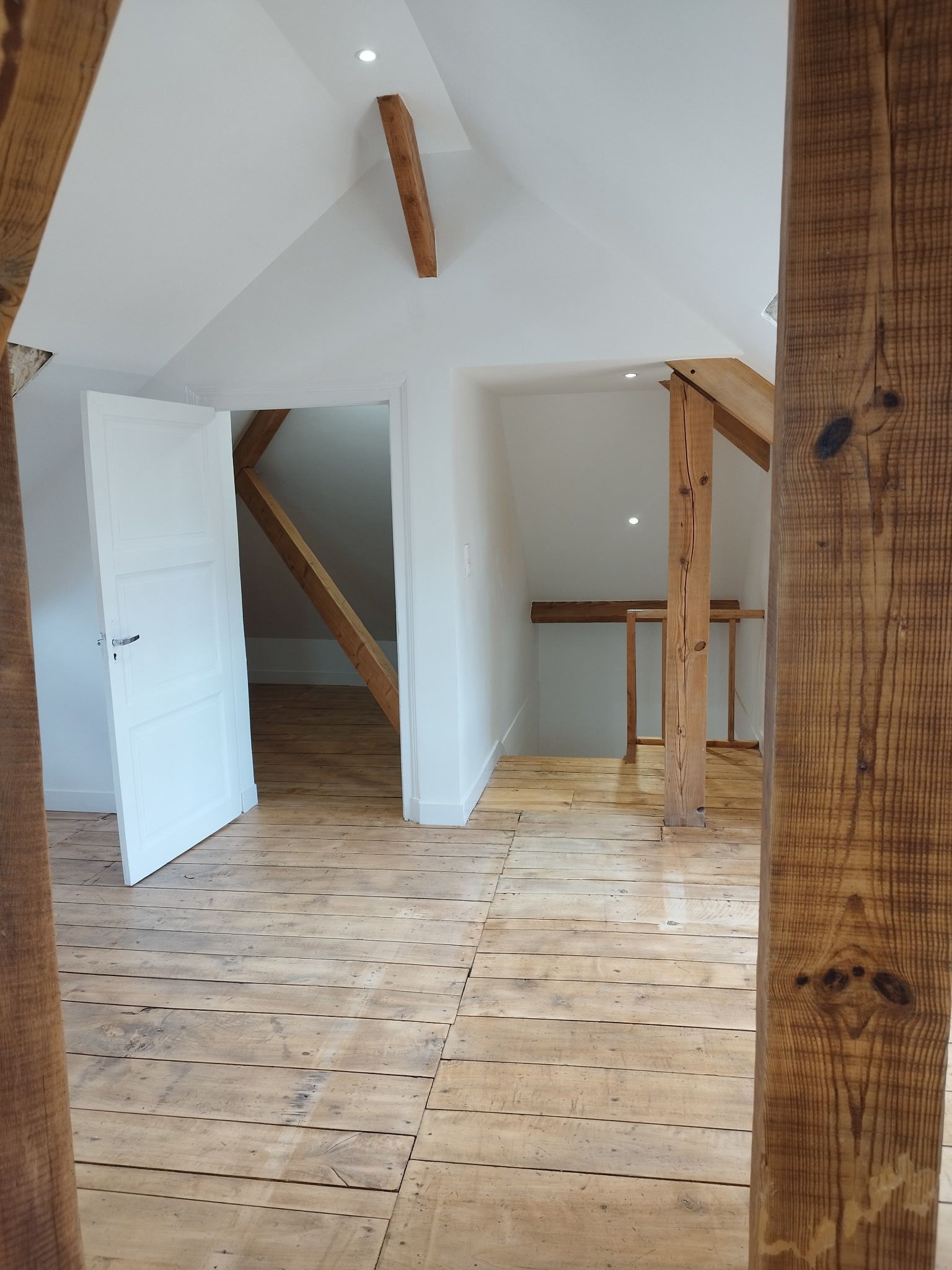 Pièce mansardée vide avec murs blancs, poutres apparentes et parquet clair.