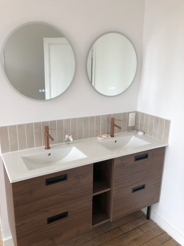 Meuble-lavabo moderne avec double vasque, miroirs ronds et armoires en bois contre un mur clair