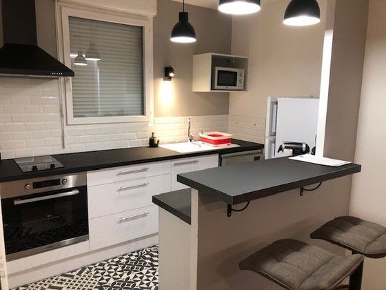 Cuisine moderne blanche avec comptoirs noirs, luminaires suspendus et un bar avec tabourets.