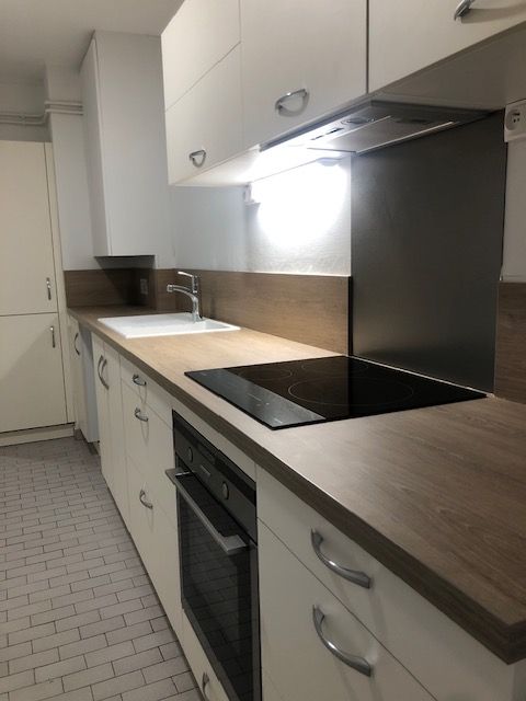 Cuisine moderne avec placards blancs, plans de travail en bois, plaque de cuisson noire et four encastré.