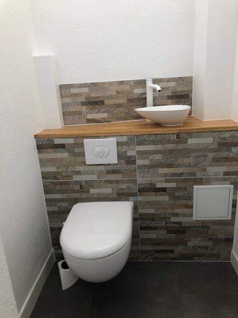 Petite salle de bains avec WC suspendu, étagère en bois et vasque blanche sur crédence carrelée.