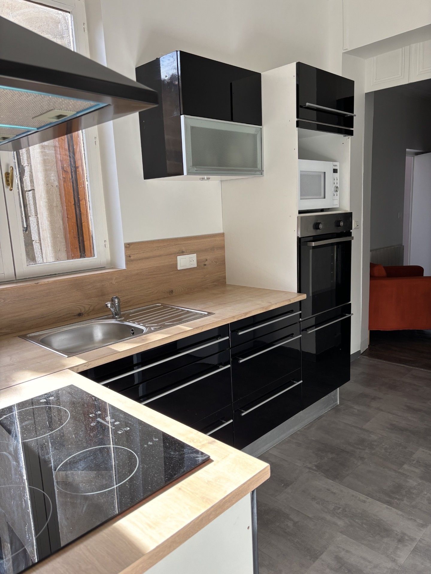 Cuisine moderne avec placards noirs, plans de travail beiges, évier en inox et four/micro-ondes intégré.