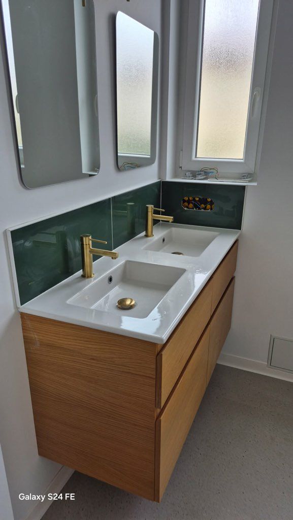 Meuble-lavabo moderne avec double vasque, robinetterie dorée et crédence carrelée verte sous des armoires à miroir.
