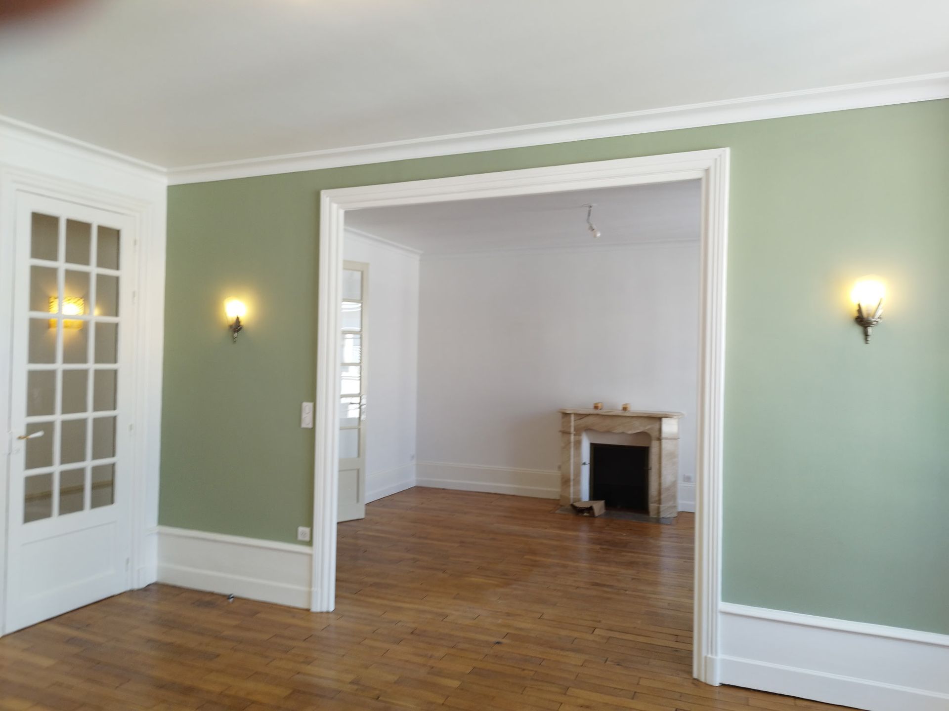 Petite chambre avec un lit, des tableaux, un bureau, une chaise et des étagères en bois dans des tons de vert et de blanc doux.