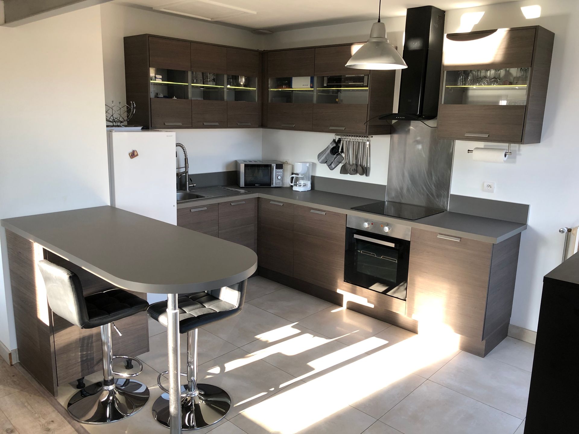 Cuisine moderne avec armoires en bois foncé, comptoirs gris, bar pour le petit-déjeuner et appareils électroménagers en acier inoxydable.