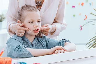 Mädchen macht Logopädie-Übungen, Therapeutin legt die Hände an seine Wangen