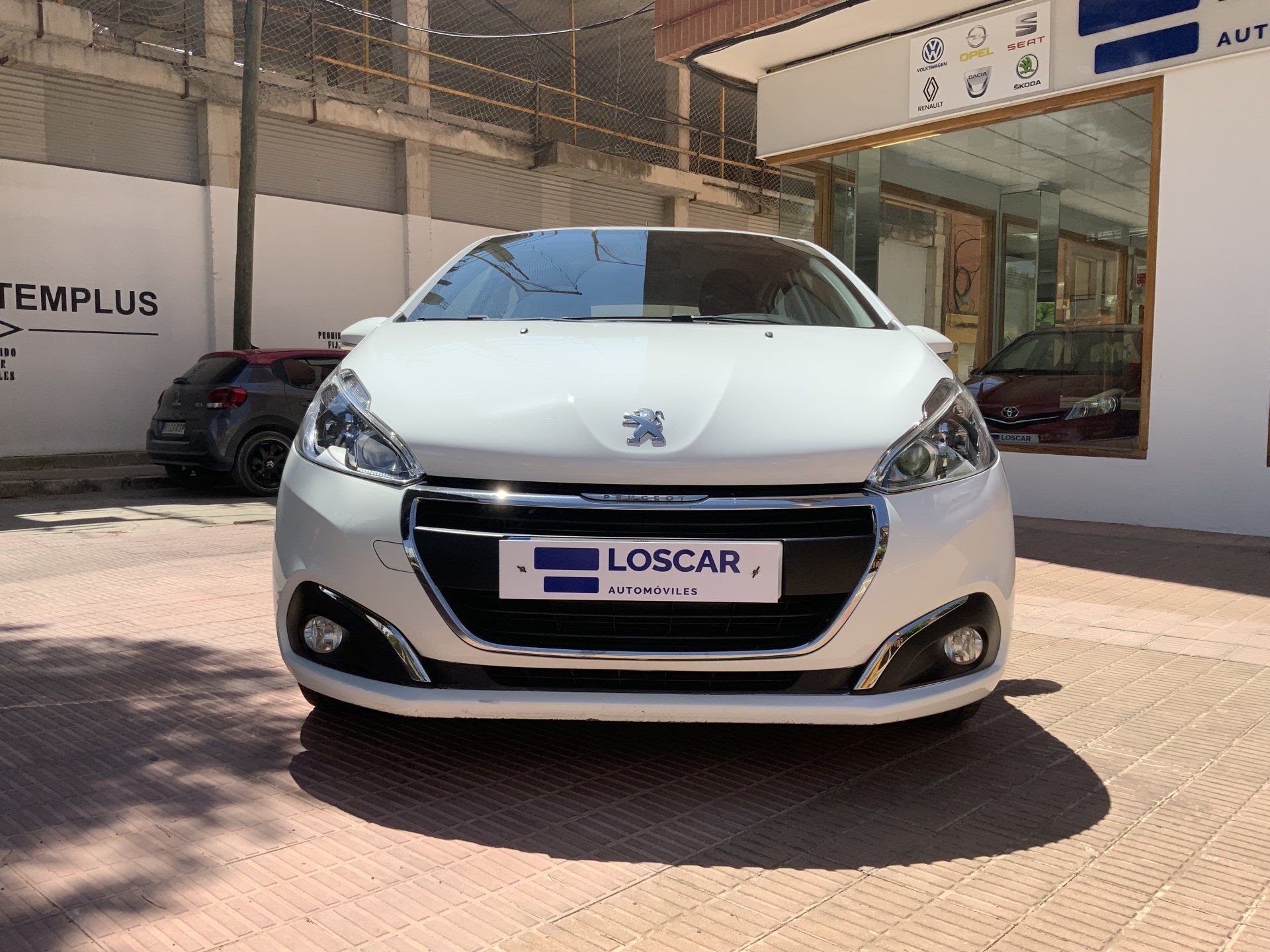 Peugeot 208 blanco estacionado frente a un edificio, con el logotipo de una empresa de alquiler de coches.