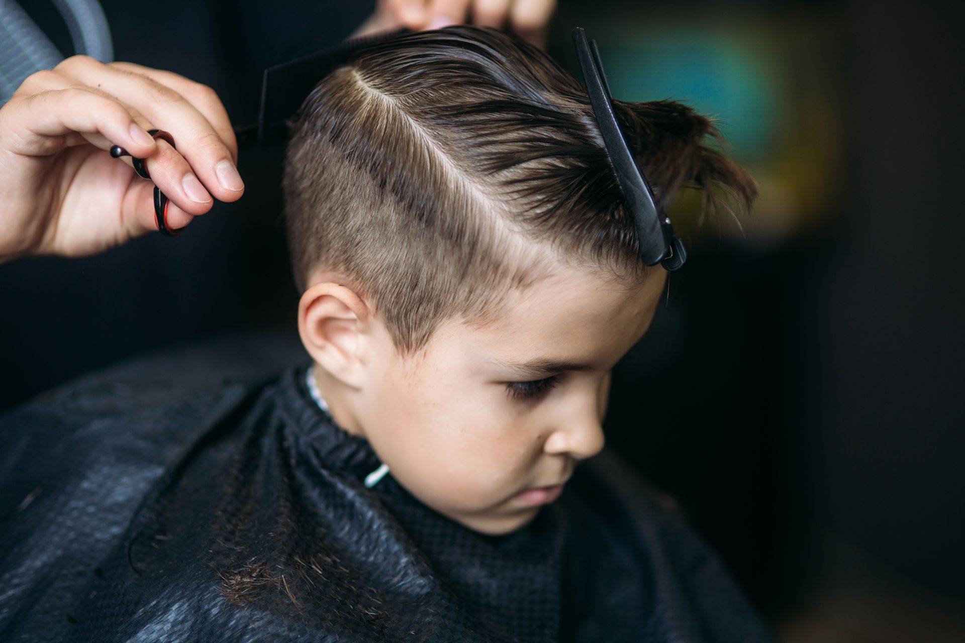 Junge bekommt einen Haarschnitt; Friseur verwendet Kamm und Schere.