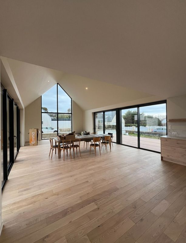 Salle à manger moderne et ouverte avec de grandes fenêtres, un parquet clair et une vue sur l'eau.