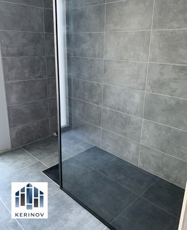 Douche moderne carrelée avec paroi en verre noir et caniveau de sol foncé.