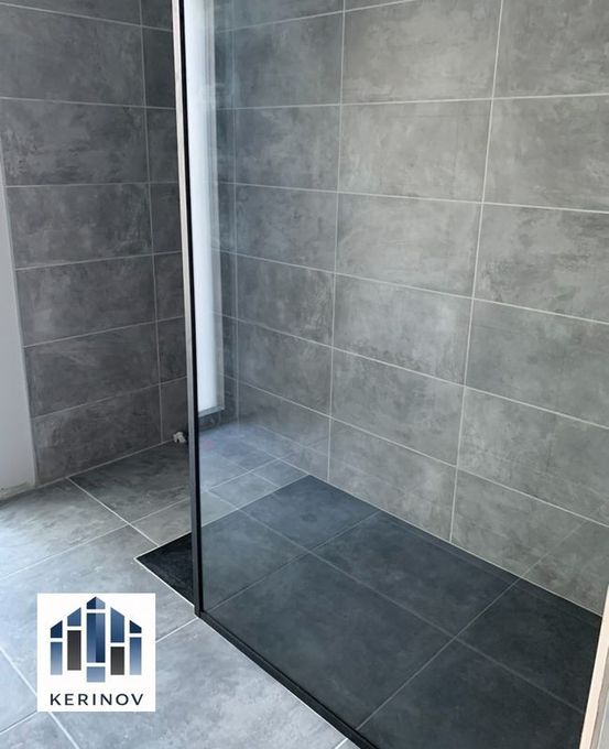 Douche moderne carrelée avec paroi en verre noir et caniveau de sol foncé.