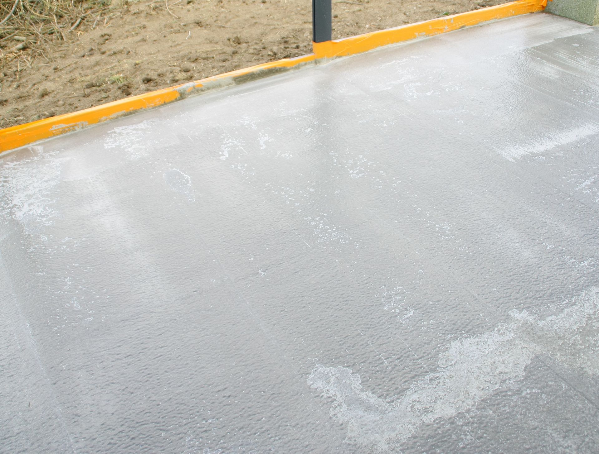 Trottoir gris mouillé le long d'un trottoir et d'une clôture jaunes, avec des taches blanches éparses en surface.