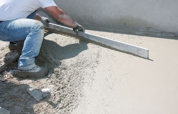 Un ouvrier nivelle du béton frais avec une longue règle sur un chantier de construction.