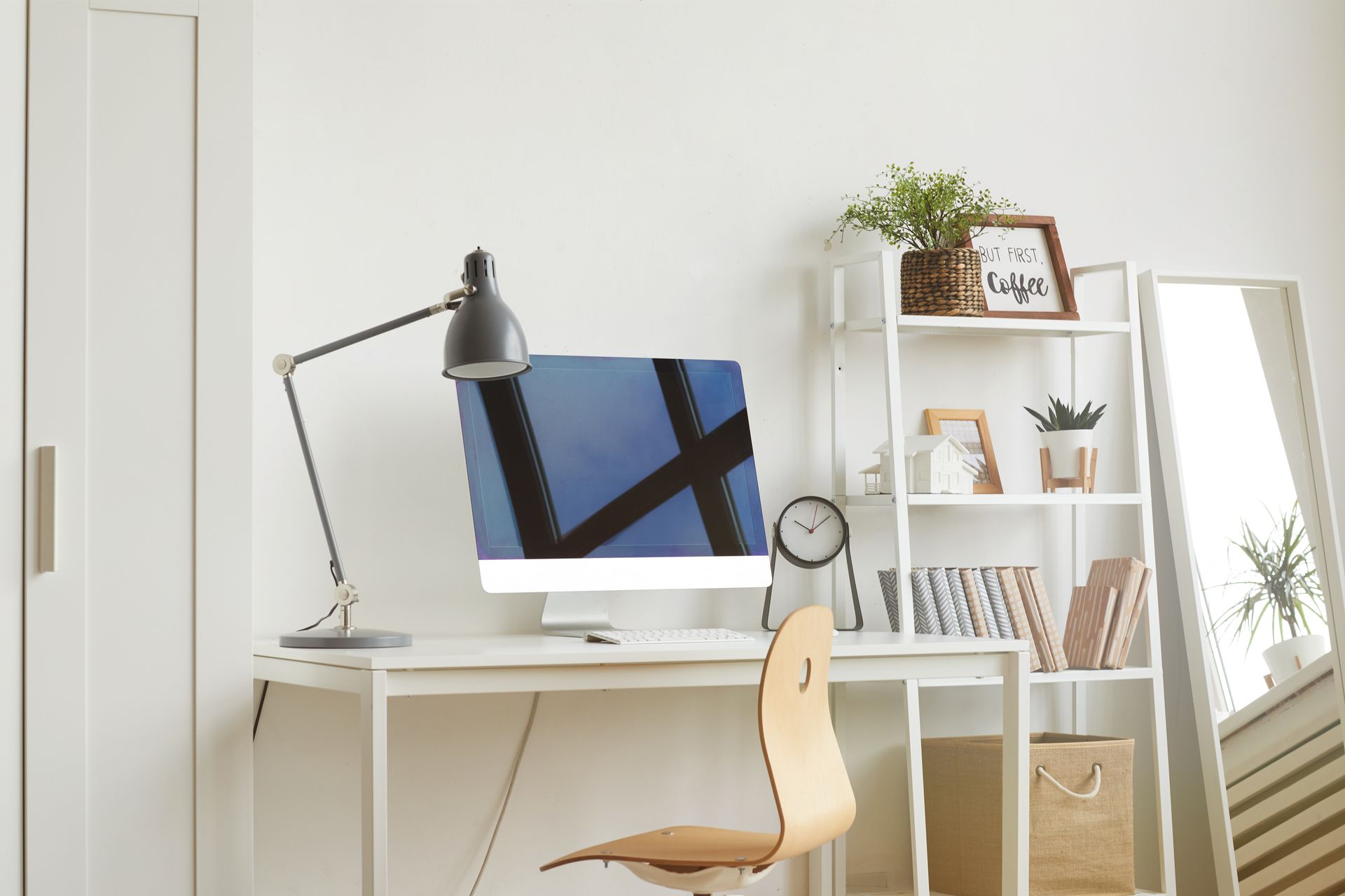 Bureau à domicile lumineux et minimaliste avec bureau, ordinateur, lampe, chaise, étagères et miroir près d'une fenêtre.
