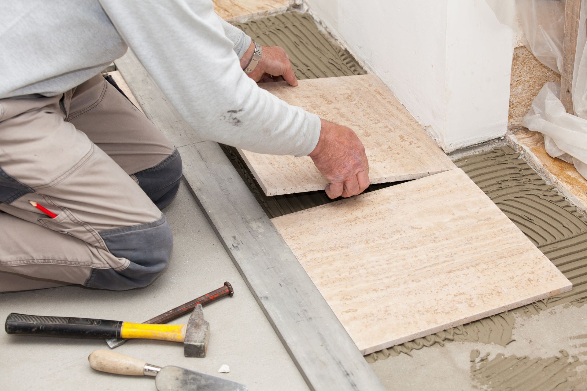 Un ouvrier pose des carreaux de sol beiges à la truelle lors de la rénovation d'une maison.