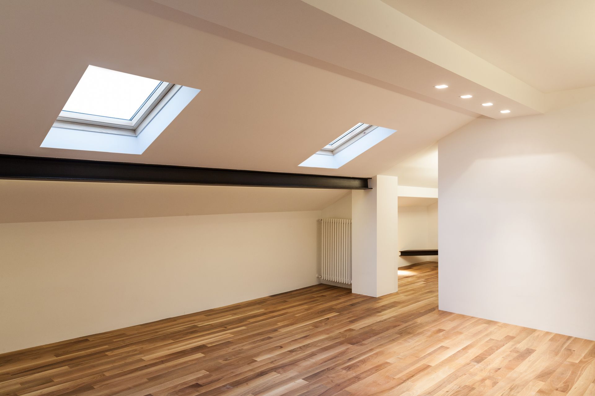 Pièce mansardée vide avec parquet, murs blancs et puits de lumière laissant entrer la lumière naturelle.