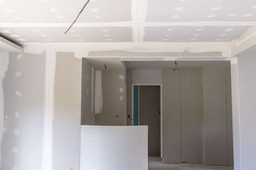 Pièce inachevée avec des plaques de plâtre réparées, un plafond apparent et une porte encastrée en construction.