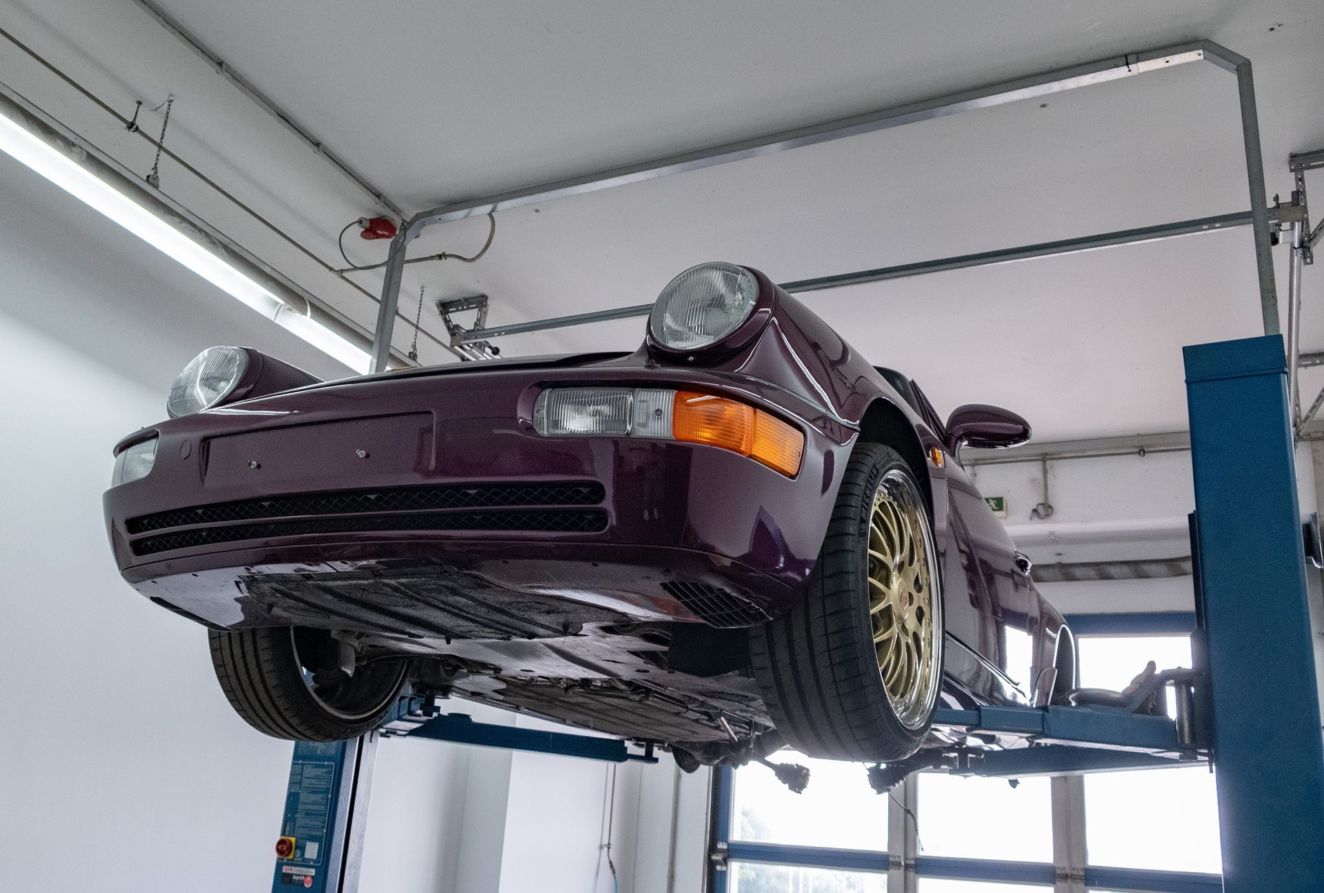 Autos auf Hebebühnen in einer großen, hell erleuchteten Autowerkstatt. Weitere Fahrzeuge und Ausrüstung sind ebenfalls zu sehen.