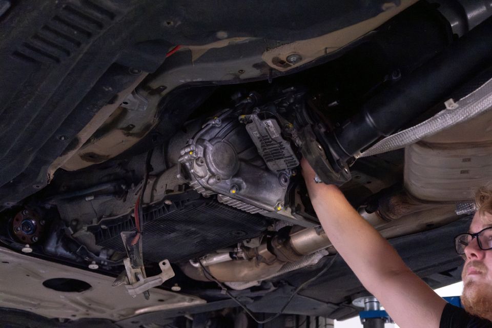 Ein Mechaniker arbeitet an der Unterseite eines Autos und greift in Richtung Getriebe.